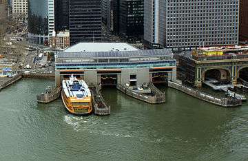 Three docks can be seen from the air, and next to them is a covered ferry terminal. This is an aerial view over a river.