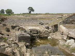 A shallow pool of water lies in front of stone blocks which were part of the port facilities of Sybaris.