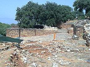 a slope on which are remains of stone walls with trees in the background