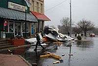 A photo of the Jamestown Cafe with a large pile of debris on the damp street in front of it. The pile is about 20' by 10' and perhaps 7' high at its peak. Much of the debris is wood and building sheet (perhaps steel?)