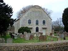 A grey-white building seen almost end-on with two storeys. The lower storey has two doors with a round-headed window between, the upper storey has three round-headed windows, and at the top is a truncated gable.