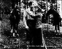 An old photo showing a woman embracing a man in front of two horses