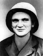 Head of a smirking man wearing a large, metal, bucket helmet and a light-colored military jacket.