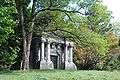 An ornate mausoleum is seen slightly obscured on the left by a tree. It has four columns around its entrance and has TRACY carved above the door. Roof comes to a point, but in layers, giving the impression of a cartoon beehive.