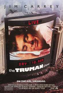 Film poster. On the side of the building is a large screen, showing a man laying his head on a pillow, eyes closed and smiling. Digital text above and below the screen state "LIVE" and "DAY 10,909", with the film's title right below it. Text at the top of the image includes the sole starring credit and text at the bottom includes the film's tagline and credits.