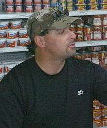 A man with a goatee wearing a black shirt and camouflage baseball cap