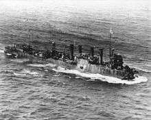 Three-quarter overhead view of destroyer with four funnels and damaged bow, at sea