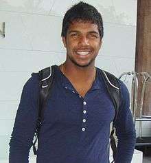 A dark coloured man in a blue shirt carrying a bag.