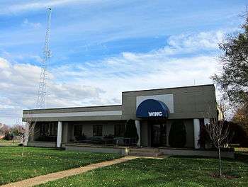 single story building among trees, radio transmitting tower to the left of building