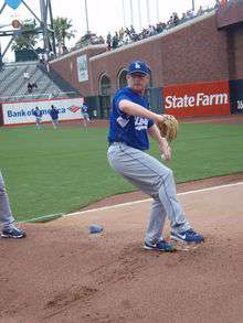 A man wearing a blue baseball jersey and cap and white baseball pants throwing a baseball with his left hand