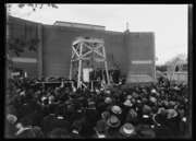 A black and white photograph of a large group of people in dark dress, mostly visible as a sea of hats, gathers around a wooden scaffolding and a partial brick wall where Secretary of State Charles Evans Hughes sets the cornerstone of National Baptist Memorial Church