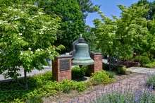 A brass bell displayed beside a sidewalk and trees